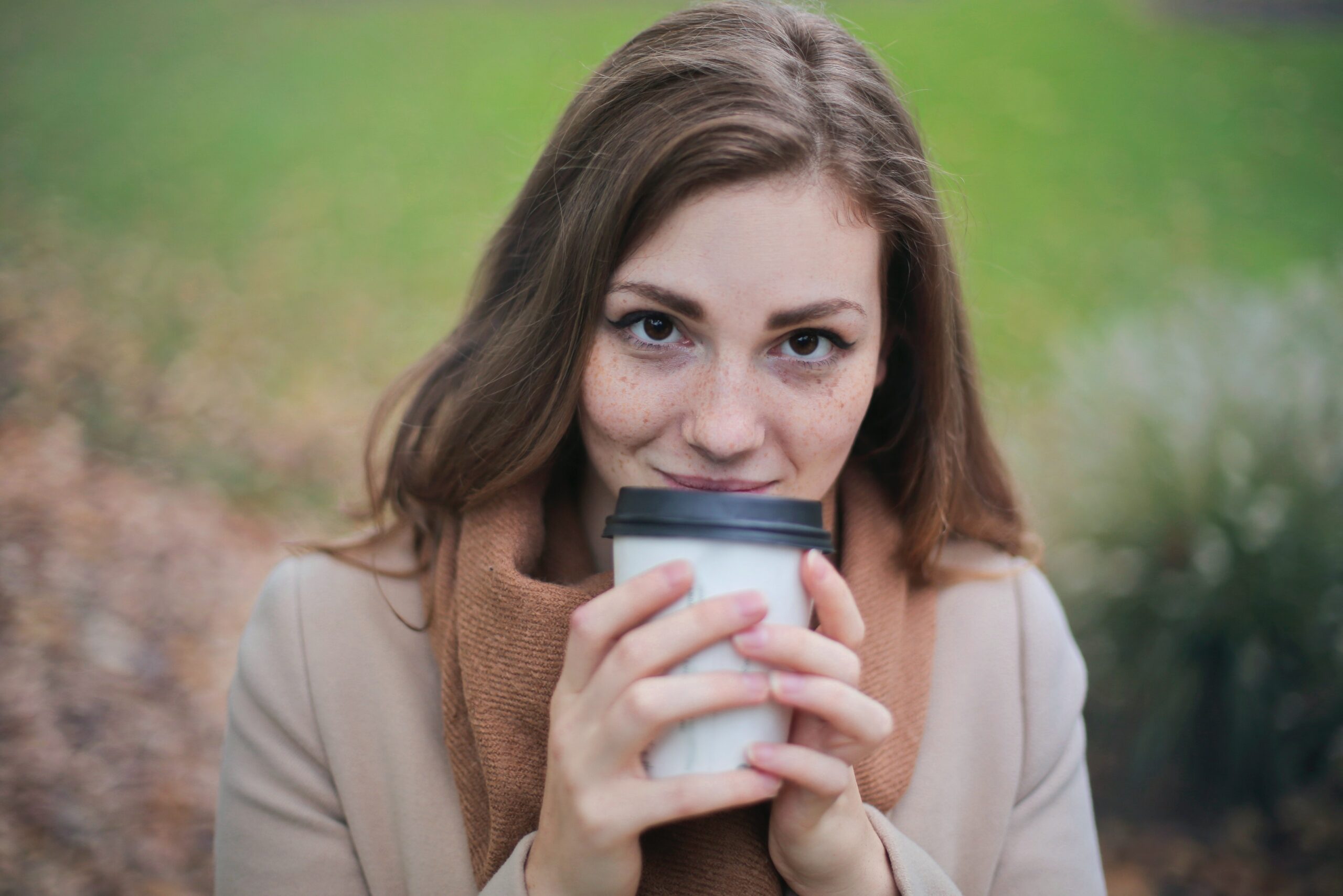 woman-in-brown-top-and-scarf-holding-a-white-and-black-travel-cup-outside