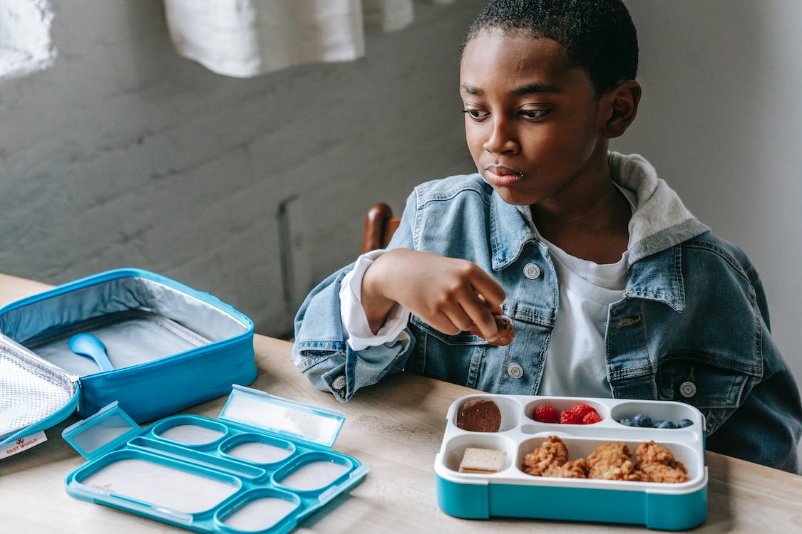 Boy eating from assorted lunch box with fruits and meat