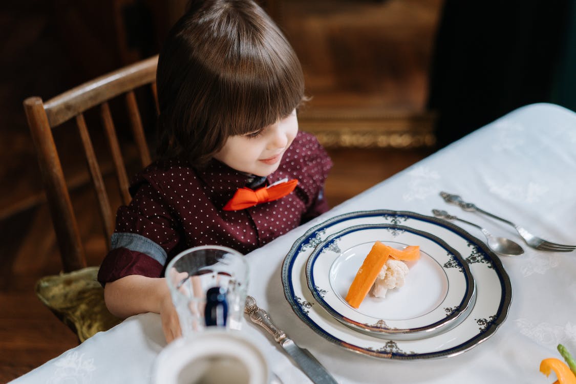 Boy smiling while looking at a small serving of carrots and broccoli on plate