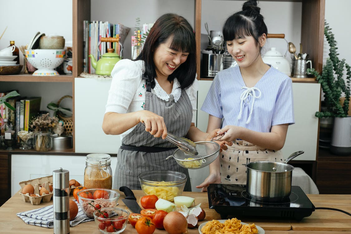 Mother and teenage daughter happily preparing food in the kitchen