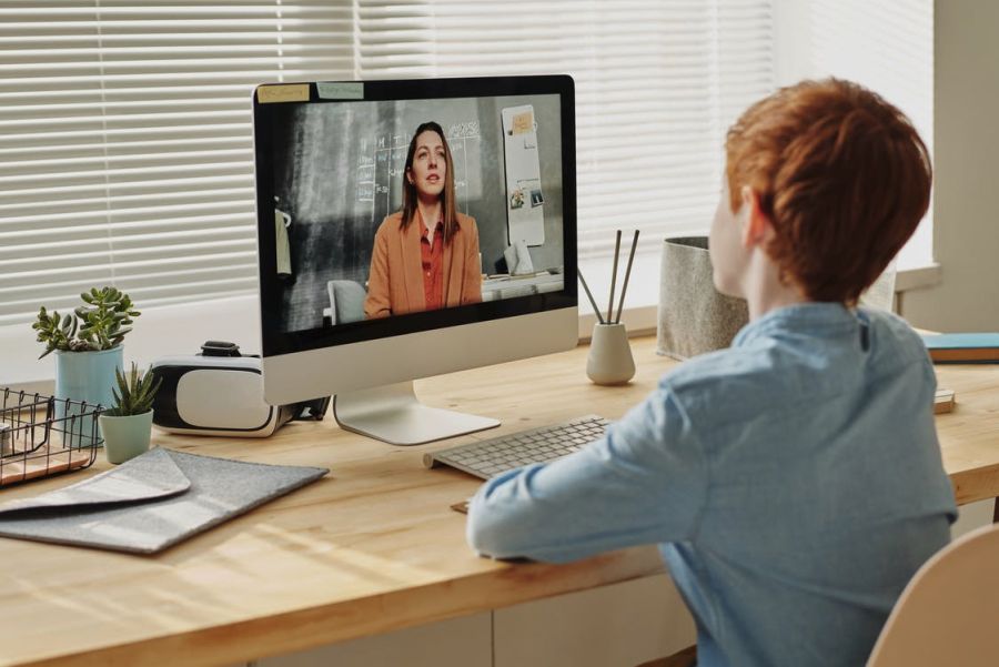 a child sitting at a table, looking at the person in the laptop in front of him