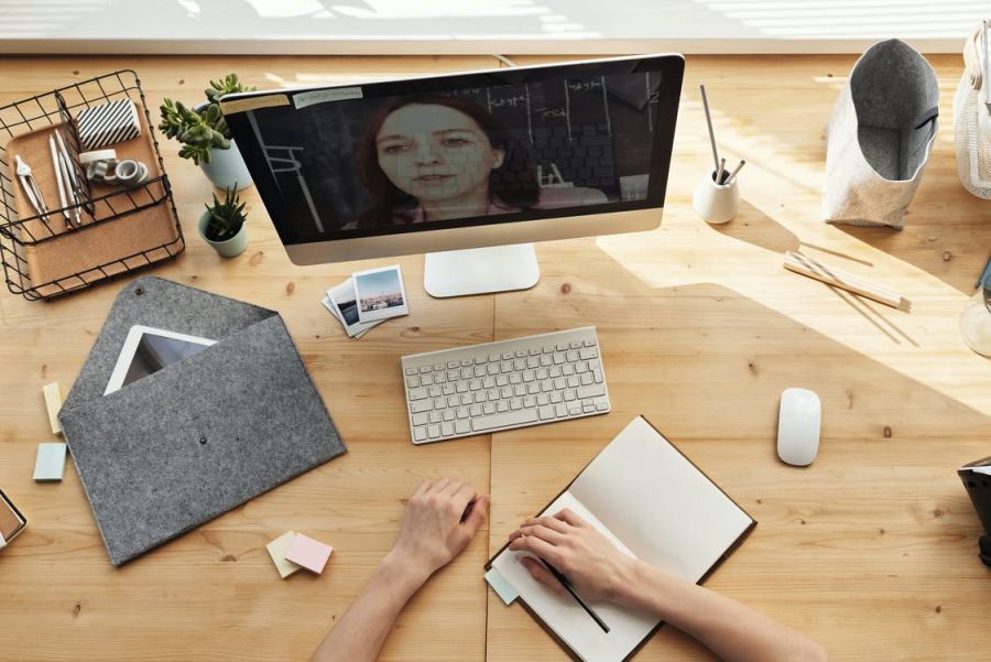 a writing desk, a laptop displaying an instructor; the desk is covered with materials used for writing