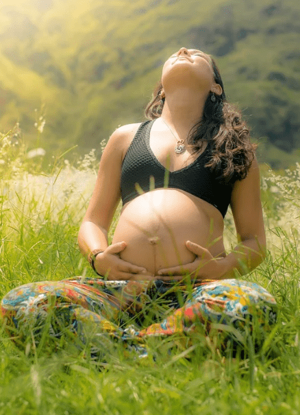 a pregnant woman sitting in the fields outdoors