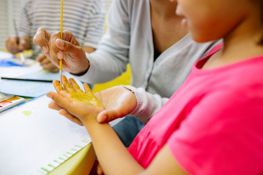 person-painting-a-girl-s-hand-with-yellow-color