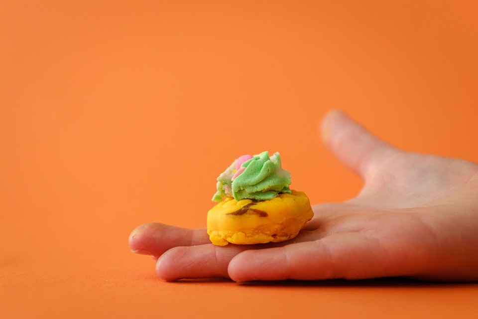 orange background, the hand of a child, cookie-shaped play-doh, yellow, green, and pink colored play-doh