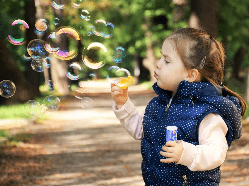 a child blowing bubbles, trees, road, leaves