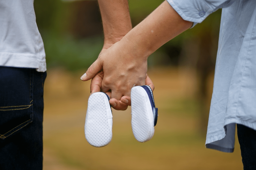 a couple holding hands with baby shoes