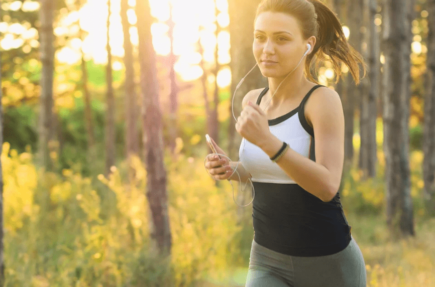 woman jogging while listening to music, bright sunny day, lots of trees and grass 