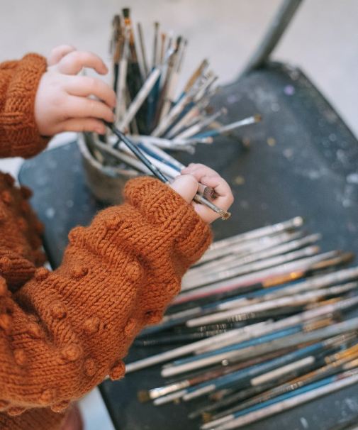 a-kid-orange-knit-sweater-holding-a-paint-brush