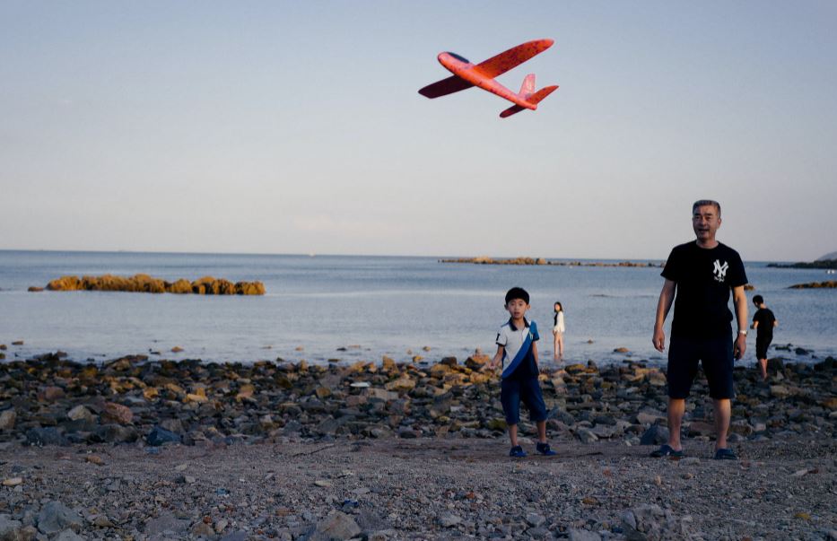 ethnic-father-and-son-launching-toy-plane-on-beach-at-sunset