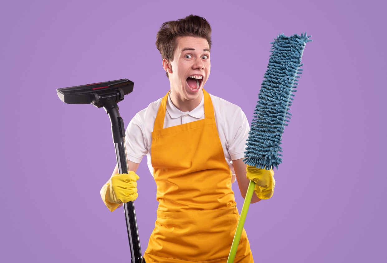 Excited housekeeper with vacuum cleaner and mop