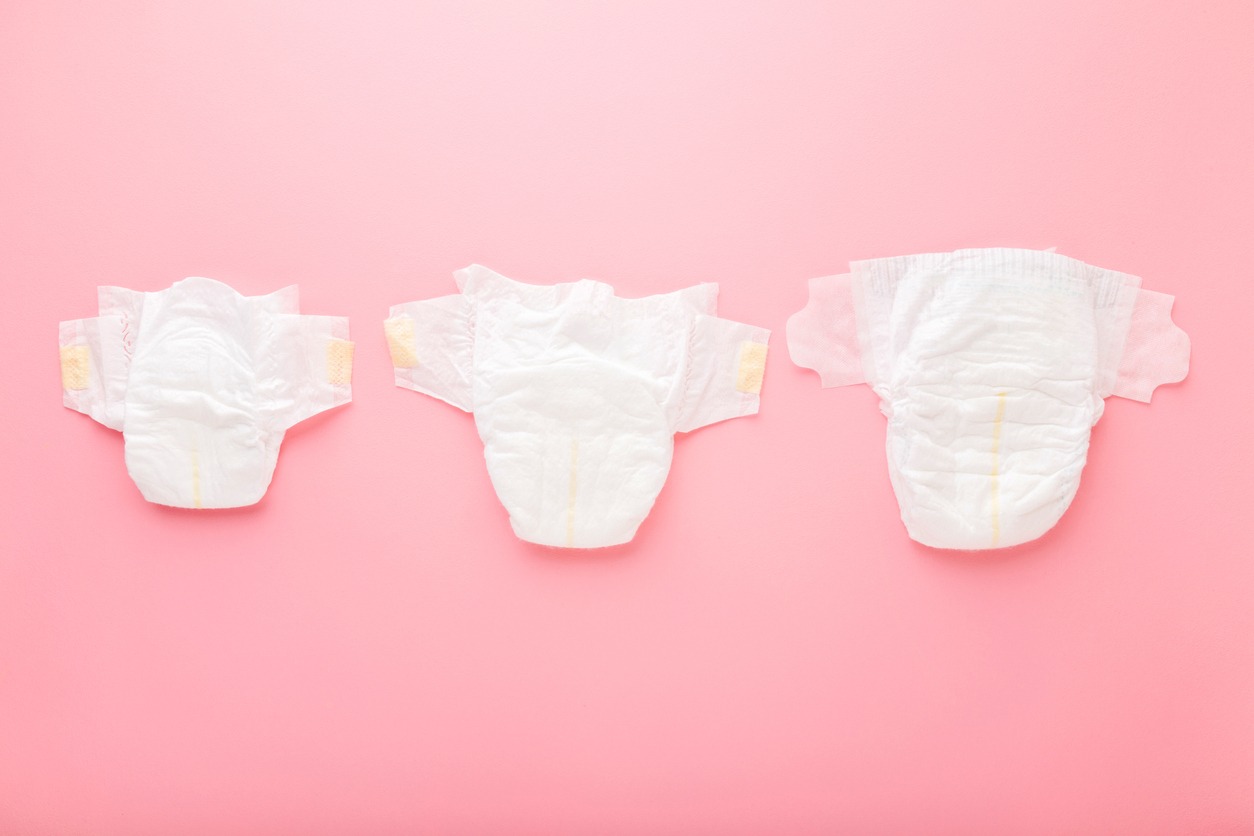 White soft baby diapers on light pink table background. Pastel color. Different sizes. Closeup. Top down view.