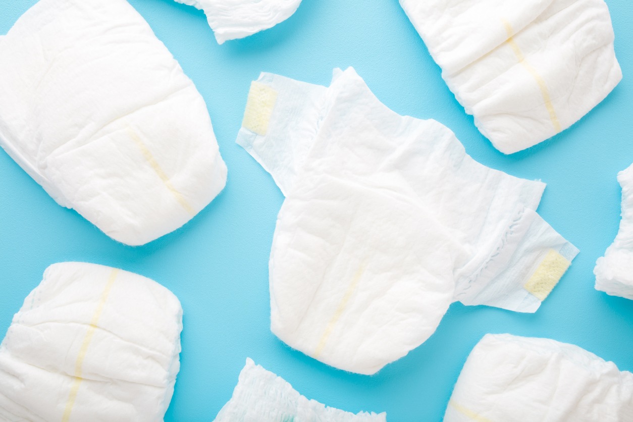 Many white baby diapers on light blue table background. Pastel color. Top down view.