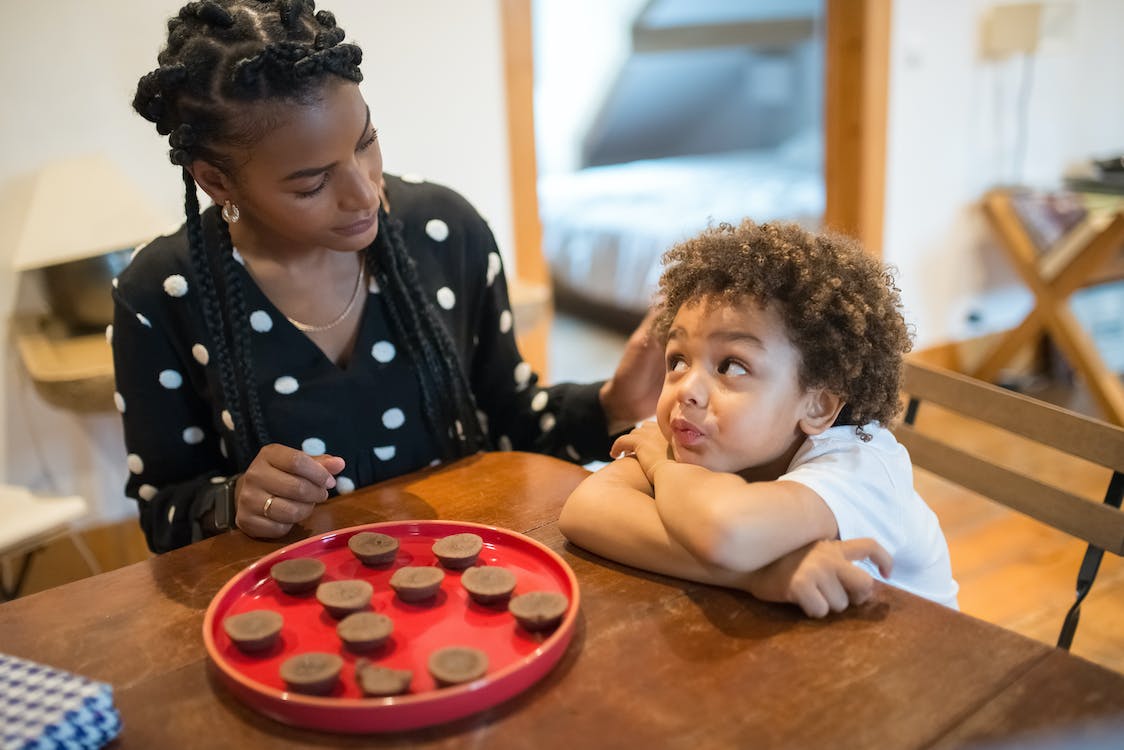Mother talking to son crossing arms with chocolates across the table